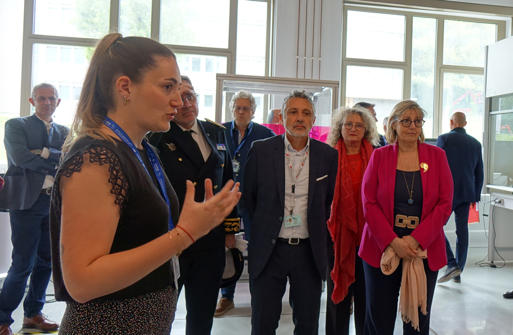 Laura Marchand, ingénieure de recherche, présente à la ministre le projet de plateforme de synthèse chimique automatisée.